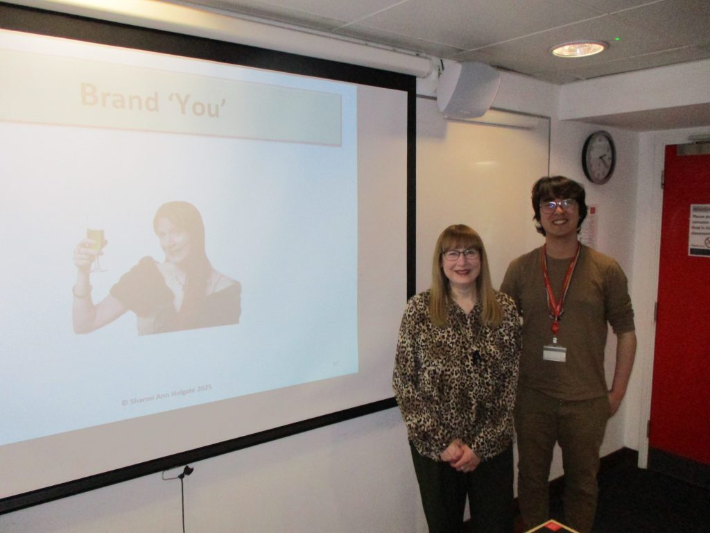 Sharon Ann with Kenji Newton standing in front of a projected slide from the training session at King's College London.