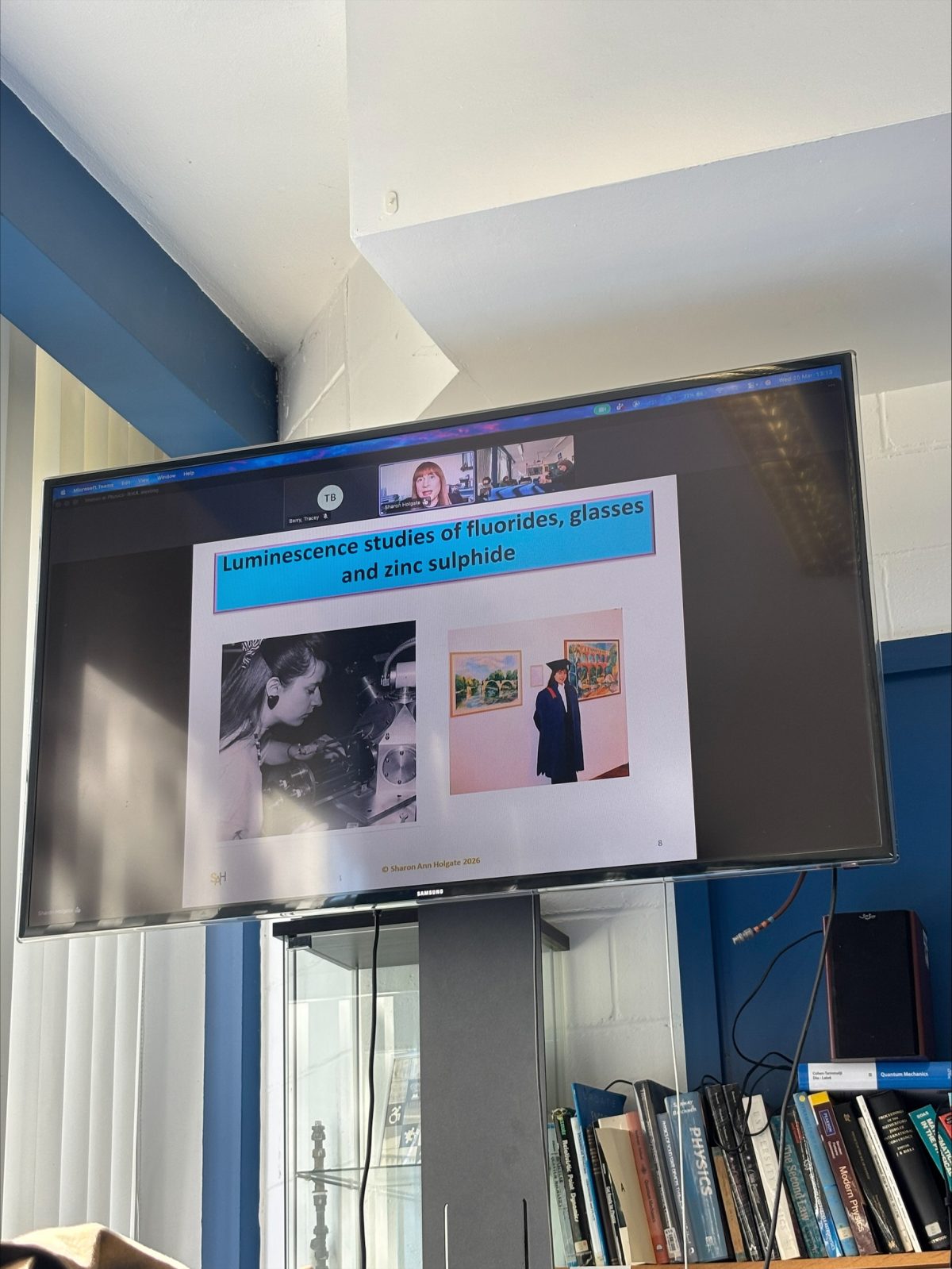 Photo taken at Royal Holloway showing Sharon Ann giving her remote talk and featuring a slide from her PowerPoint presentation showing photos of her as a DPhil student in the lab and on graduation day.